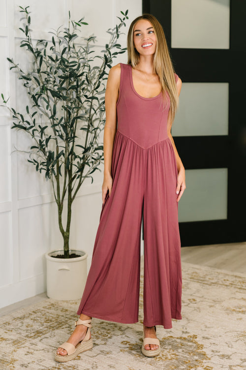 Woman wearing a mauve jumpsuit standing indoors with a plant in the background