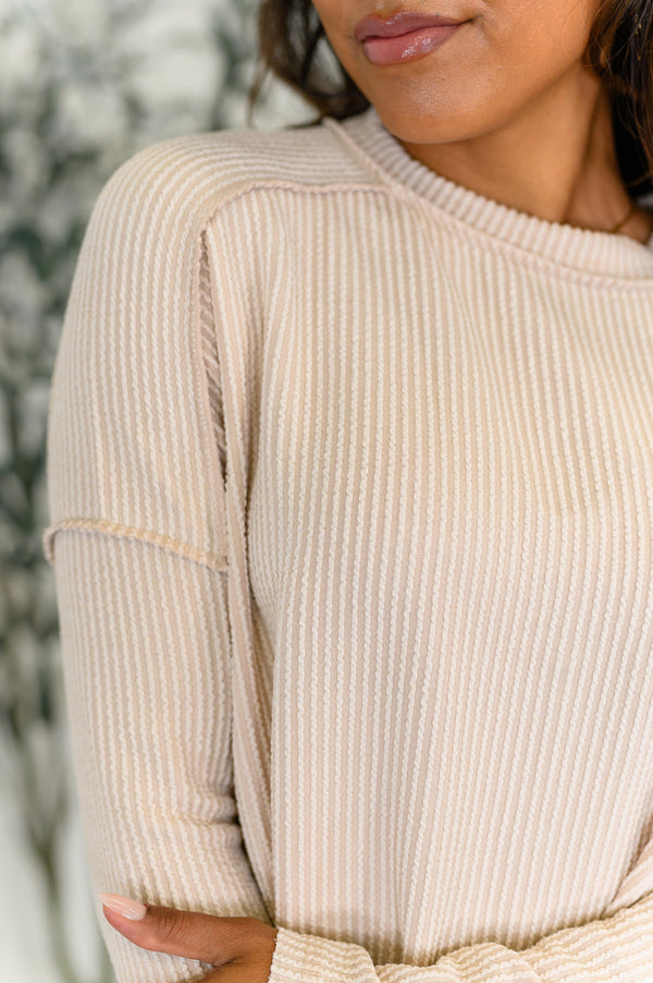 Close-up of a person wearing a beige ribbed sweater with a blurred background