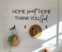 Decorative wall with 'Home sweet home, thank you, God' text, hat, bag, and plant.