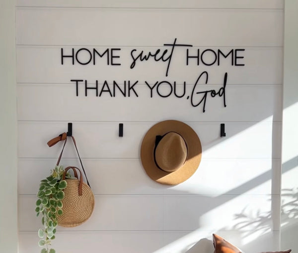 Decorative wall with 'Home sweet home, thank you, God' text, hat, bag, and plant.